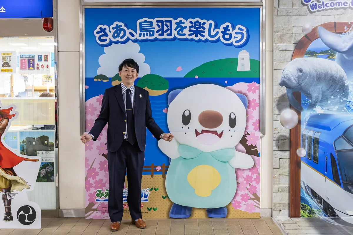鳥羽駅にあるミジュマルの看板と撮影する寺家さん
